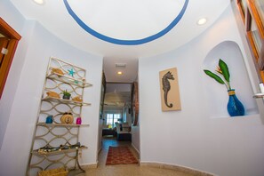 A hallway with a decorative metal shelf, a seahorse painting, and a blue vase on the wall. - Paradise!   Luxury Condo w/Rooftop Pool in Premier Community (Roatan)