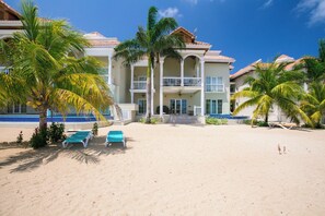 A beachfront property with a pool, palm trees, and two lounge chairs. - Paradise!   Luxury Condo w/Rooftop Pool in Premier Community (Roatan)