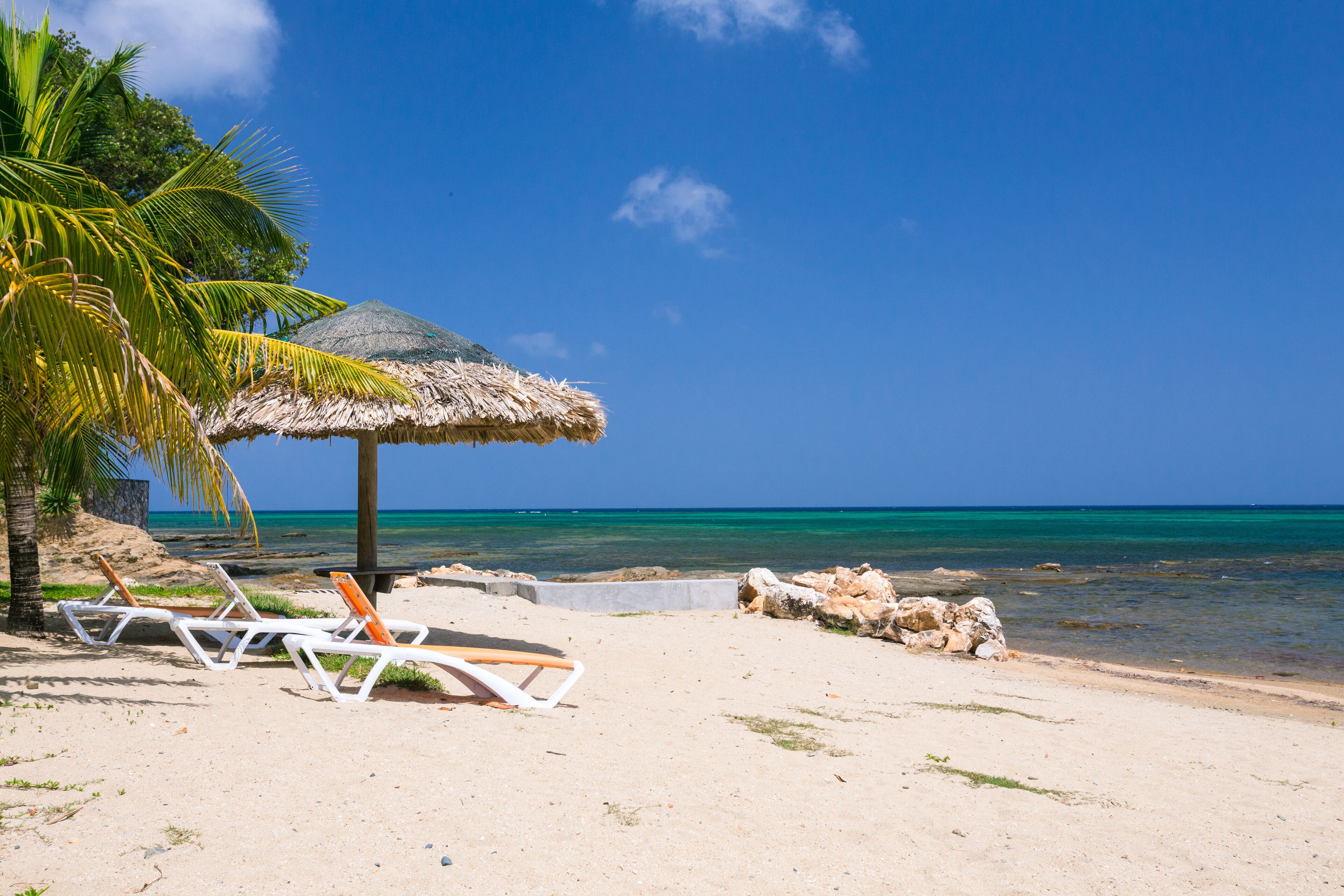 Uma praia com cadeiras de praia e um guarda-sol de palha.