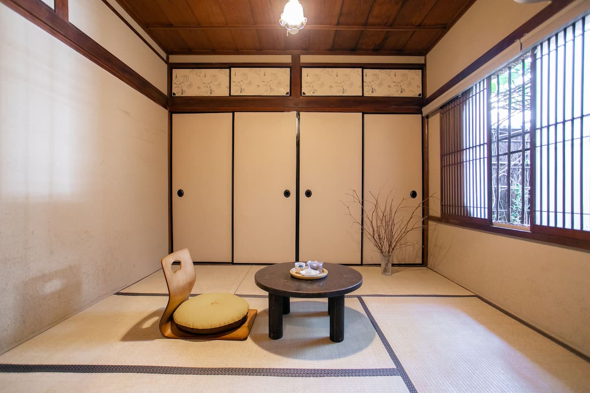 Ein traditioneller japanischer Raum mit Tatami-Böden, einem niedrigen Tisch mit Tablett, einem gepolsterten Sessel und Schiebetüren.