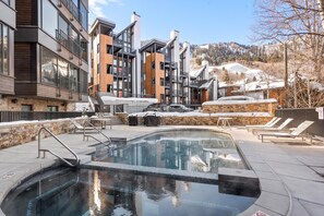 A modern hotel with a heated outdoor pool, stone walls, and a view of snow-covered mountains. - Cozy Cute Mountainside Ski-In-Ski-Out Studio (Aspen)