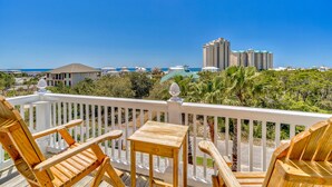 A wooden deck with chairs and a table, overlooking a beach and buildings.