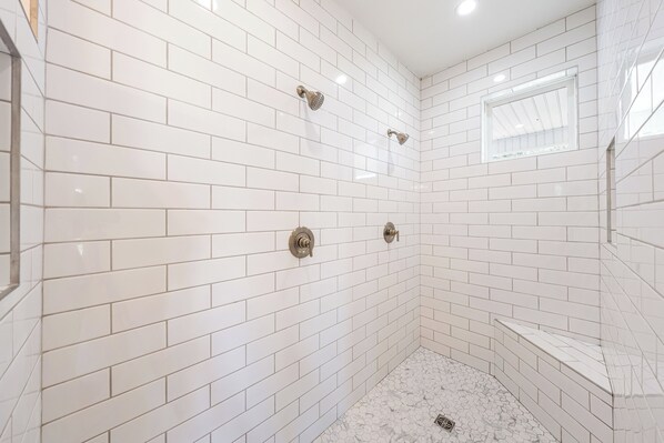 Un baño con azulejos blancos tipo metro, una ducha con cabezal de ducha manual y una ventana pequeña.