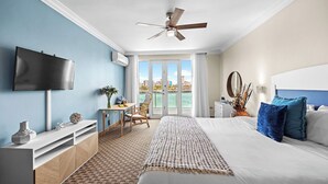 A hotel room with a bed, a desk, a chair, a TV, and a view of the ocean.
