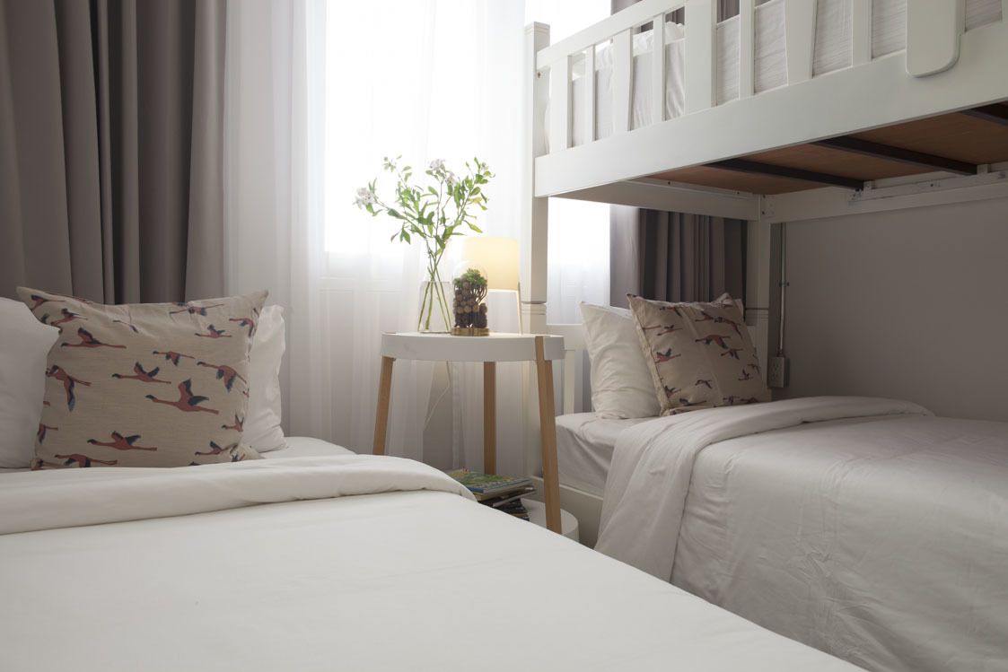 A hotel room with two beds, a small table with a vase of flowers, and a window with curtains.