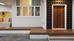 Une entrée moderne avec une porte en bois, une grande fenêtre avec des rideaux et un petit espace extérieur aménagé pour s’asseoir.