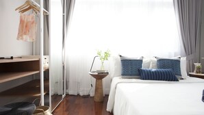 Une chambre à coucher comprenant un lit, une table de chevet, un portant à vêtements et une fenêtre avec des rideaux.