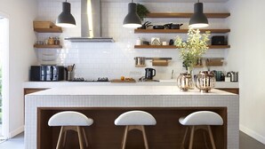 Une cuisine moderne dotée d’un grand îlot central, de luminaires suspendus et d’étagères en bois.