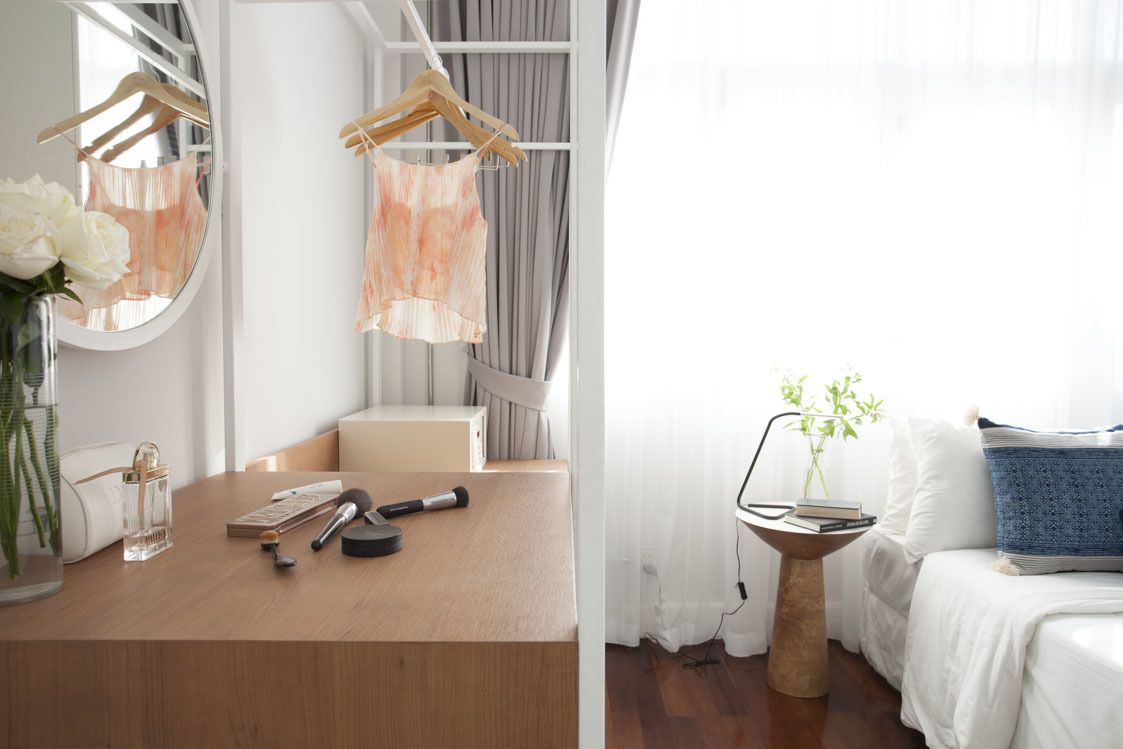 A modern bedroom with a wooden dresser, a mirror, a hanging robe, and a bedside table with a lamp and books.