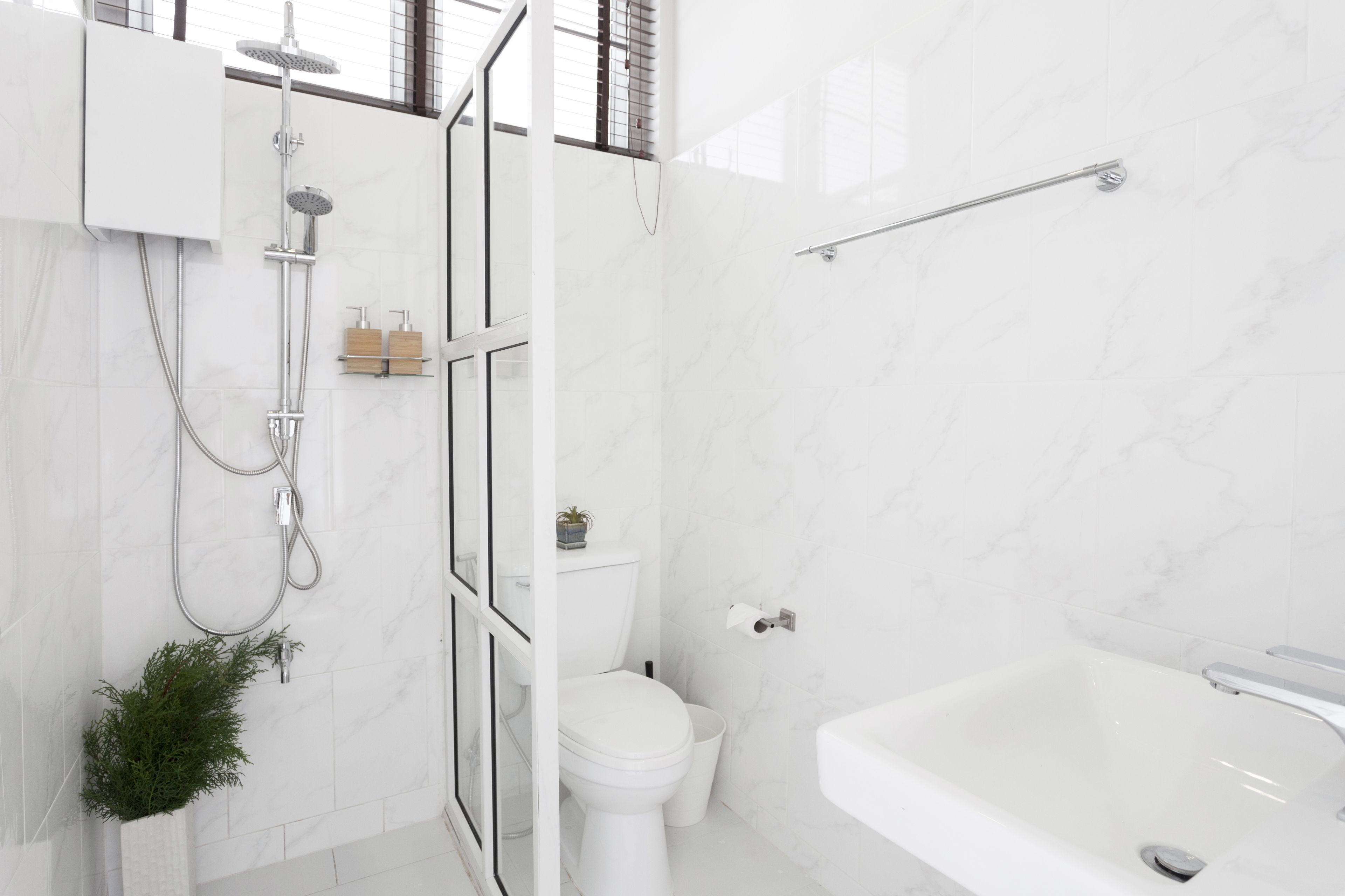A modern bathroom with a white marble wall, a glass shower enclosure, a white toilet, and a white bathtub.