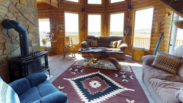 A cozy cabin interior with a stone wall, a fireplace, a large window, and a comfortable seating area. - Juniper Ridge 5 BR Family Cabin (Blanding)