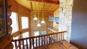 A wooden cabin interior with a stone wall, wooden beams, and hanging pendant lights. - Juniper Ridge 5 BR Family Cabin (Blanding)
