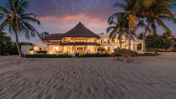 A beachfront resort with a thatched-roof structure, palm trees, and a sandy beach.