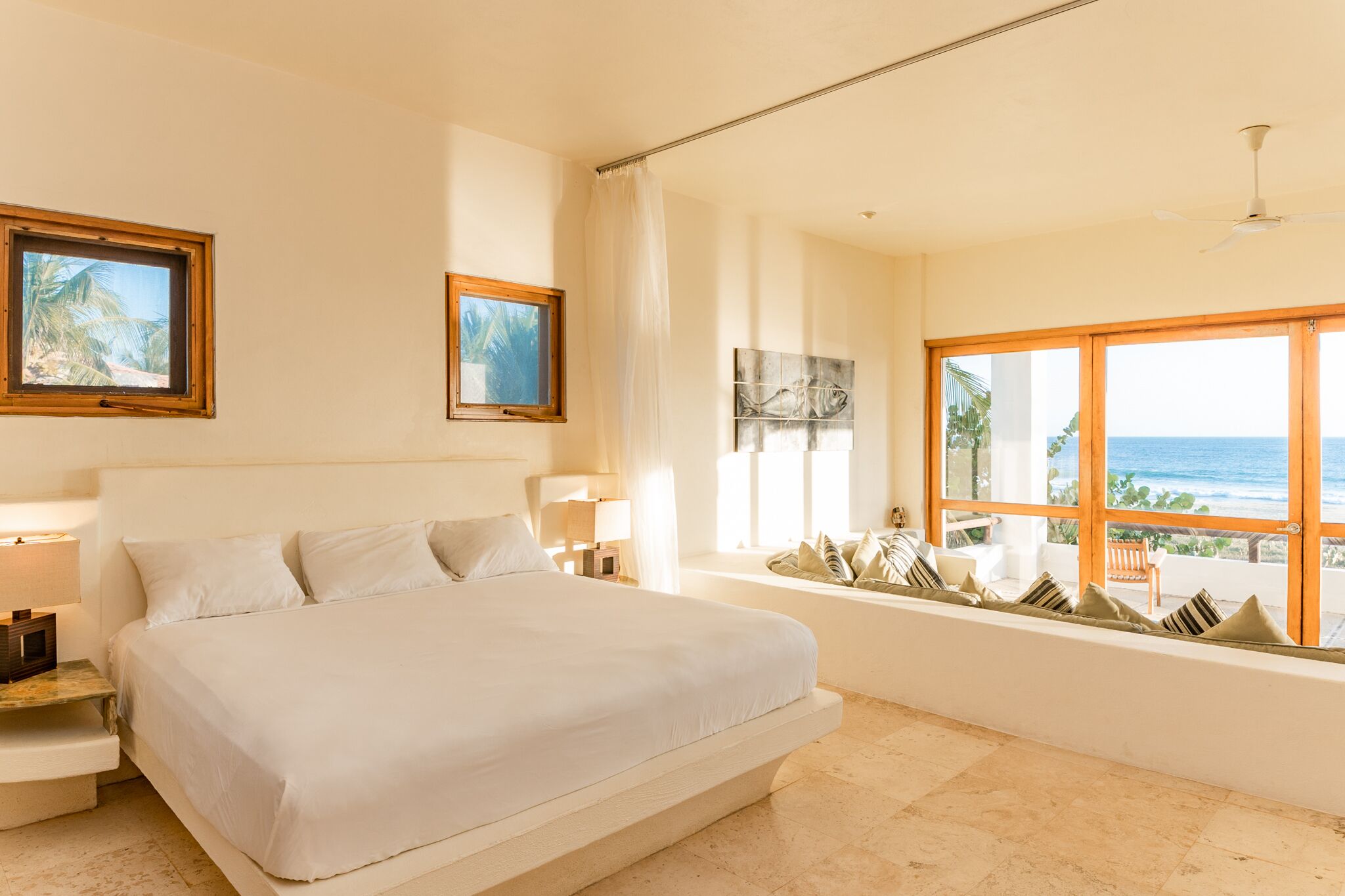 A large bed with a view of the ocean, a ceiling fan, and artwork on the walls.