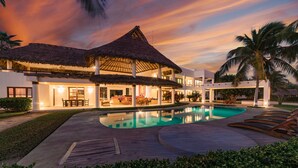 A resort with a swimming pool, thatched-roof structures, and palm trees.
