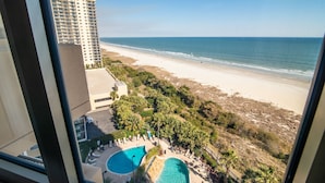 A view of a beach resort with a pool area, palm trees, and a high-rise building in the background. - $150 activities - E-gift card when you book - Luxury, Oceanfront Retreat - 2 King Beds | M804 (Myrtle Beach)