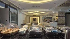 A hotel breakfast area with buffet stations, a seating area, and a kitchen in the background. - Best Smyrna Hotel (Kusadasi)