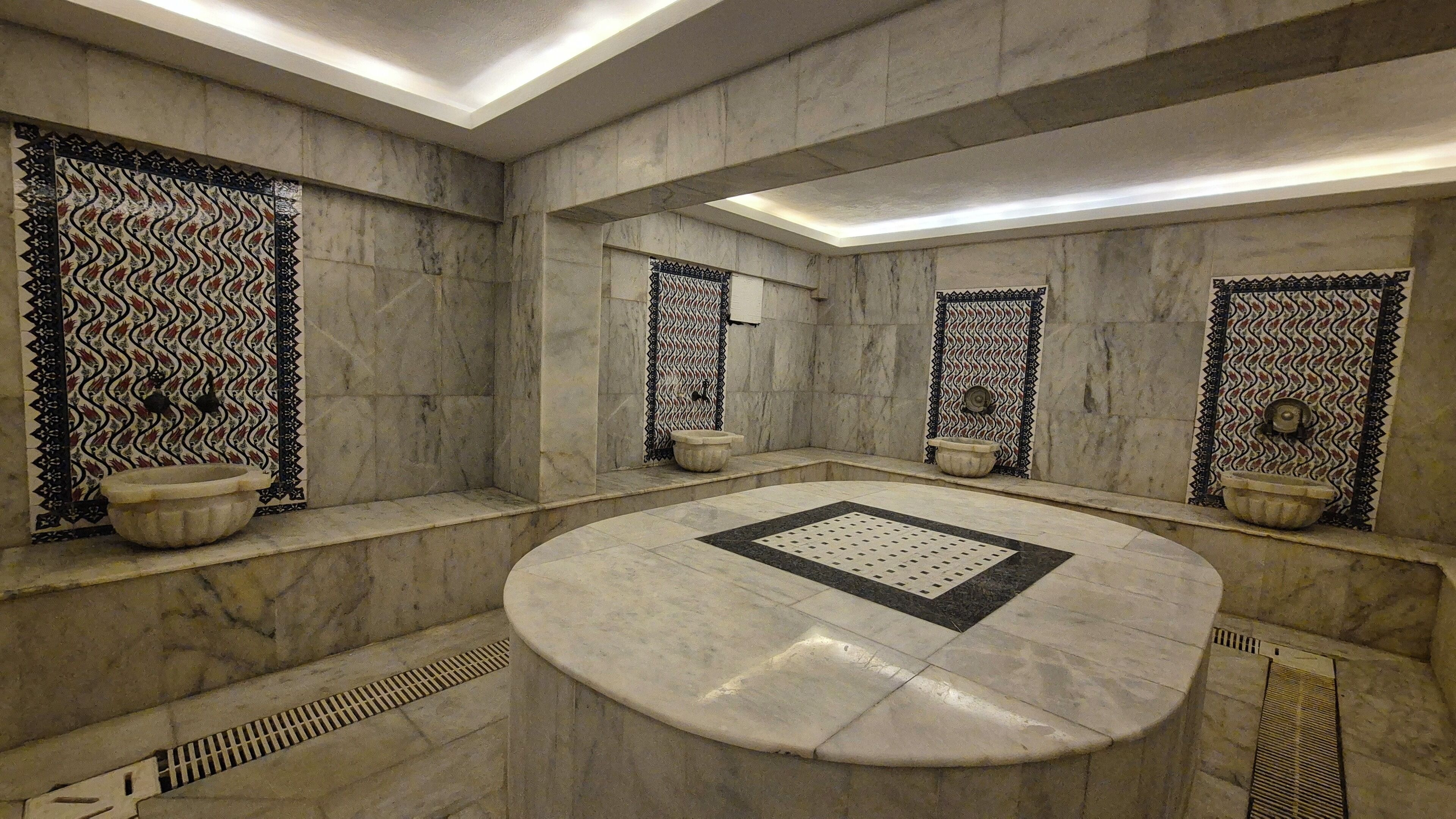 Een moderne badkamer met een centraal rond badkamermeubel, meerdere douches en decoratieve betegelde wanden.