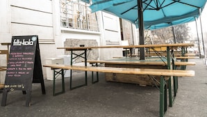 Outdoor tables and chairs under a blue canopy, with a chalkboard menu listing food items. - Madama Hostel & Bistrot (Milan)