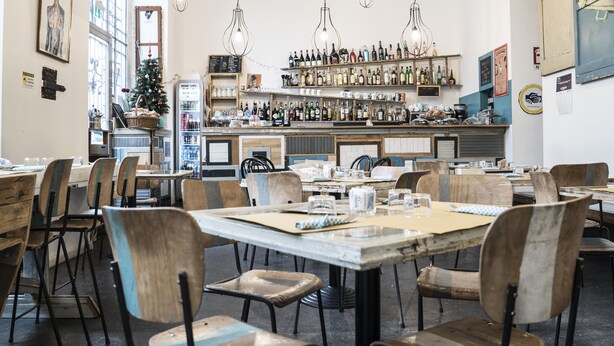 A restaurant with wooden tables and chairs, a bar area with shelves of bottles, and a Christmas tree. - Madama Hostel & Bistrot (Milan)