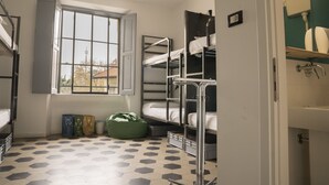 A dormitory room with bunk beds, a window, a tiled floor, and a bathroom with a sink and toilet. - Madama Hostel & Bistrot (Milan)