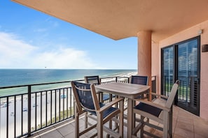 A balcony with a table and chairs, overlooking a beach and the ocean.