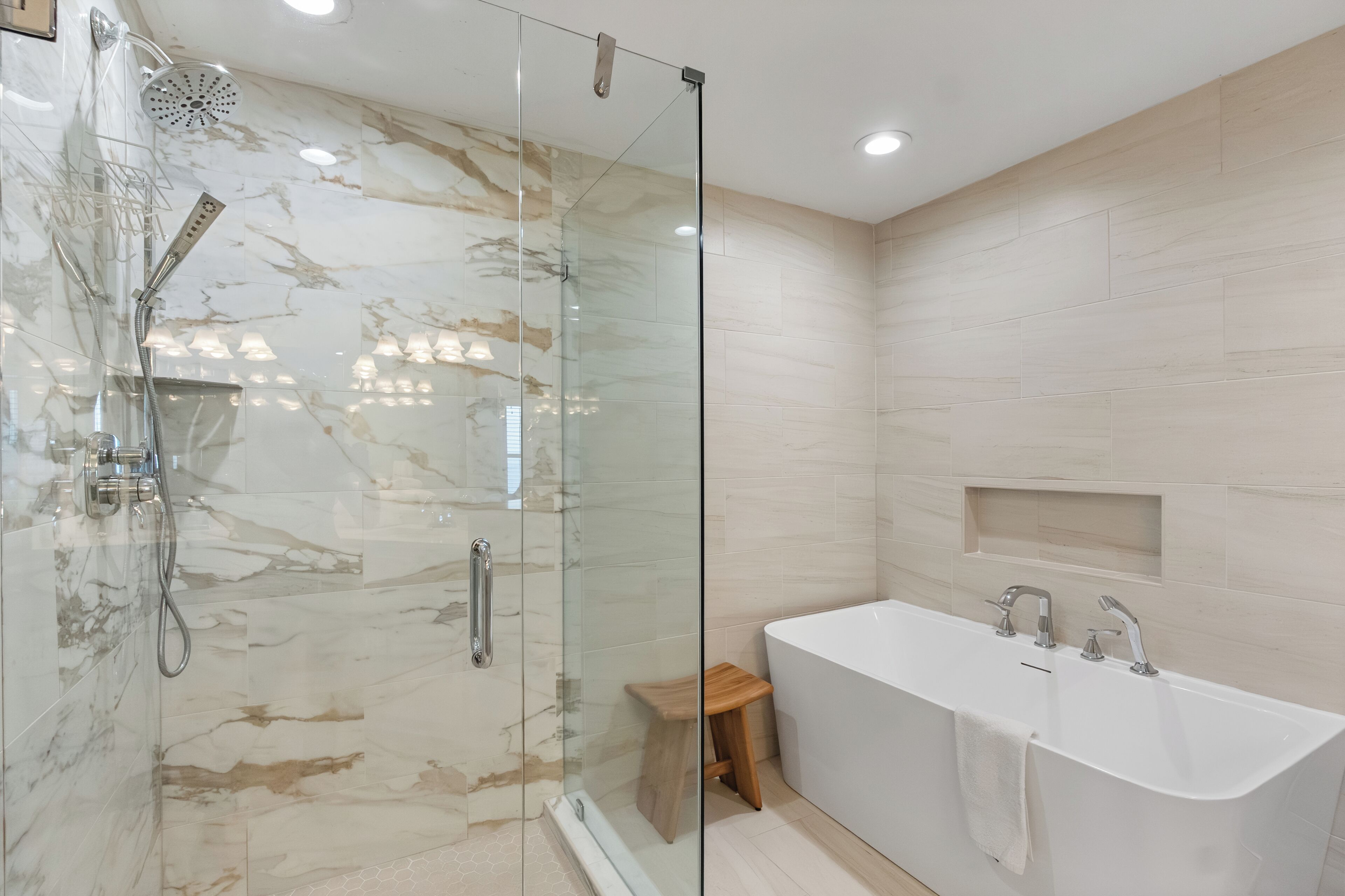 A modern bathroom with a glass-enclosed shower, a wooden stool, and a freestanding bathtub.