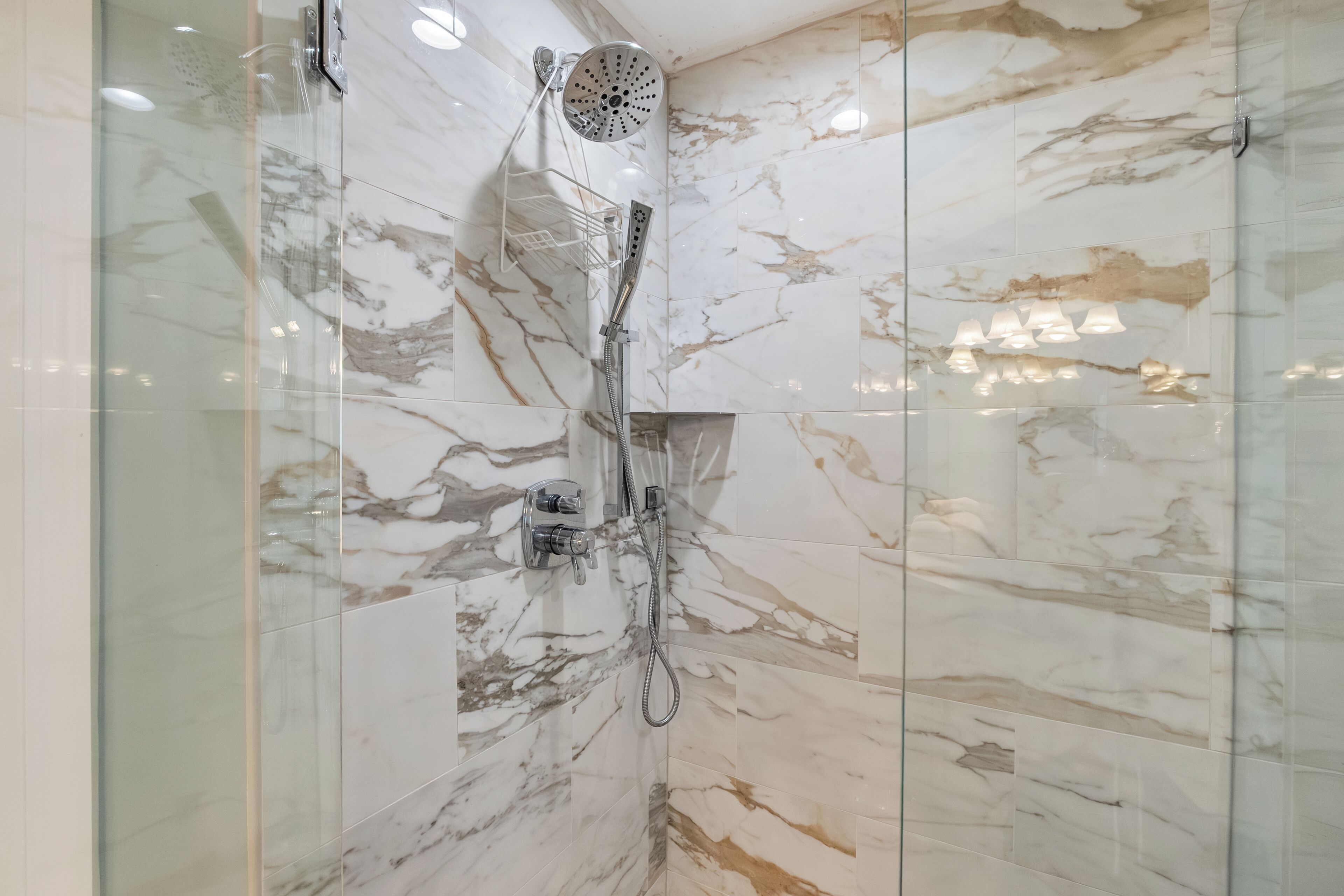 A bathroom with marble walls, a glass shower enclosure, and a handheld showerhead.