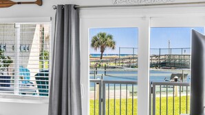 A room with a view of a beach, a palm tree, and a fence.
