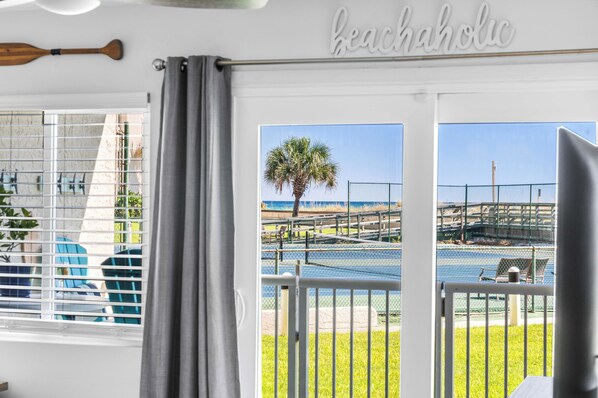 A room with a view of a beach, a palm tree, and a fence.