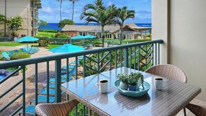 A balcony with a table, chairs, and a view of a pool and beach. - H206 Ocean View Suite - Modern and Clean - Sleeps 6 in Air Conditioned Comfort! (Kapaa)