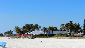 Una propiedad frente a la playa con un edificio grande, palmeras y una playa de arena.