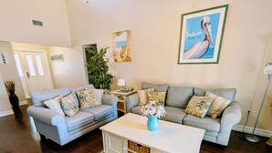 Un salon avec deux canapés gris clair, une table basse blanche et un vase bleu contenant des fleurs.