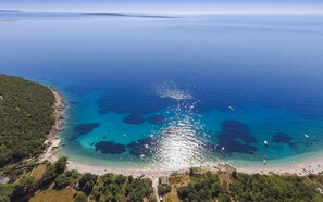 Une vue aérienne d’une zone côtière, avec une eau d’un bleu limpide, une plage de sable et une végétation luxuriante.