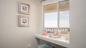 Una stanza con una finestra che si affaccia su un balcone, uno sgabello e due quadri appesi al muro.