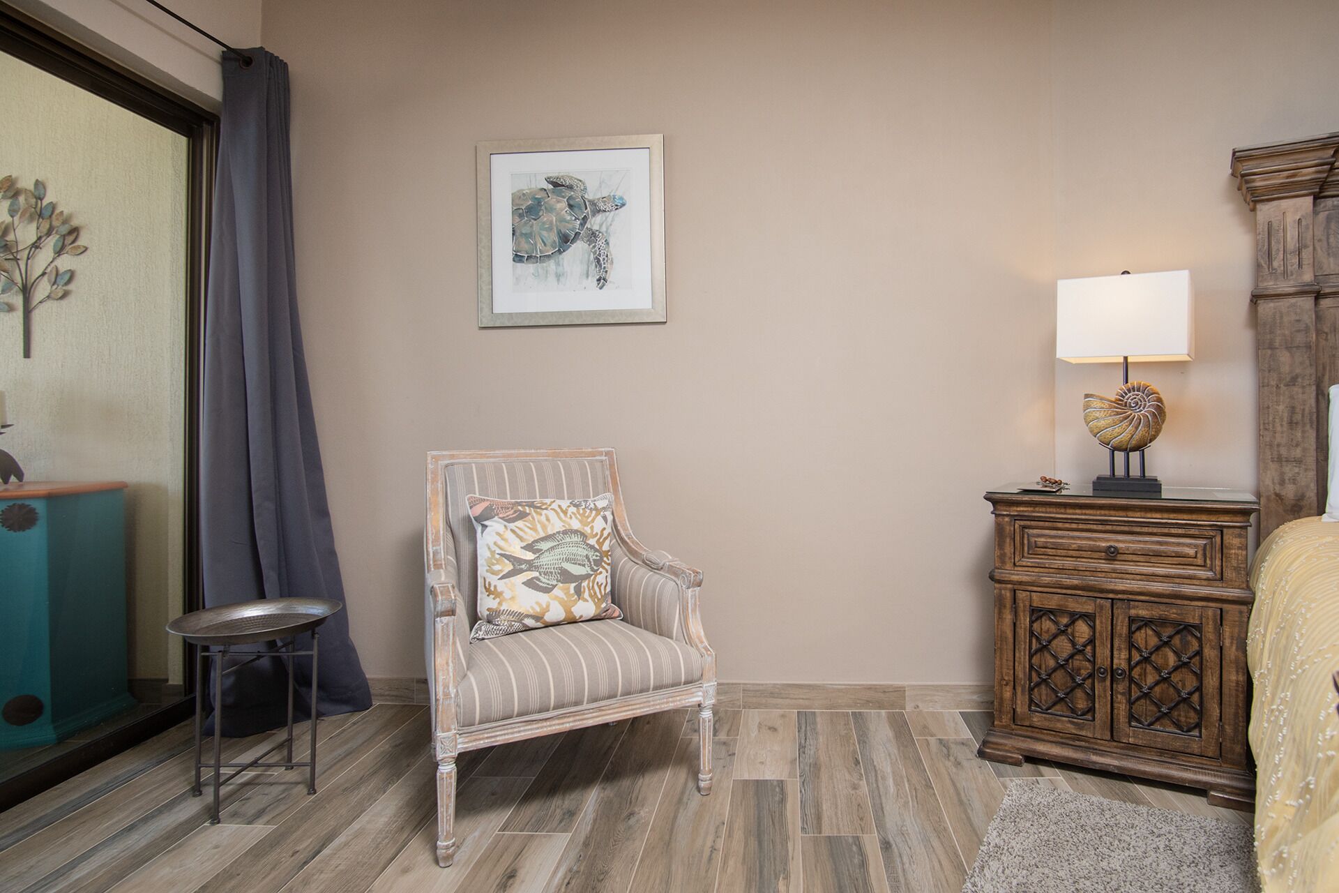 A room with a striped armchair, a small table, a cabinet, and a framed artwork on the wall.