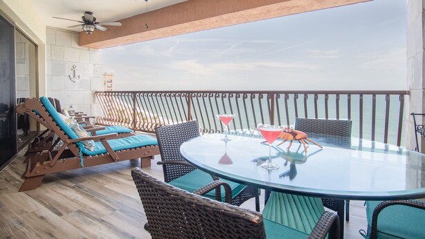 Un balcone con mobili in vimini, un tavolo in vetro e vista sull'oceano.