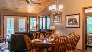 A dining area with a wooden table set for six, surrounded by wooden chairs. There is a ceiling fan above the table, and a chandelier hanging from the ceiling. - Grand View - Mountain Views, Pool Table, Fire Pit (Banner Elk)