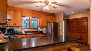 A kitchen with wooden cabinets, a large island with stools, a refrigerator, and a ceiling fan. - Grand View - Mountain Views, Pool Table, Fire Pit (Banner Elk)