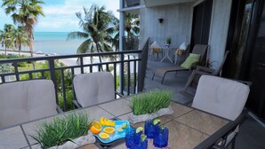 Un balcon avec une table préparée pour prendre un verre, une chaise et une vue sur l’océan.