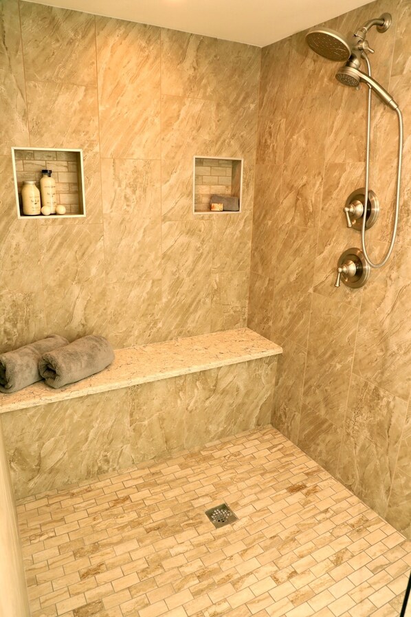 A bathroom with a shower, a towel rack, and two small shelves with toiletries.
