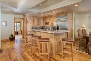 Una cocina moderna con armarios de madera, un refrigerador de acero inoxidable y una zona con taburetes de bar.