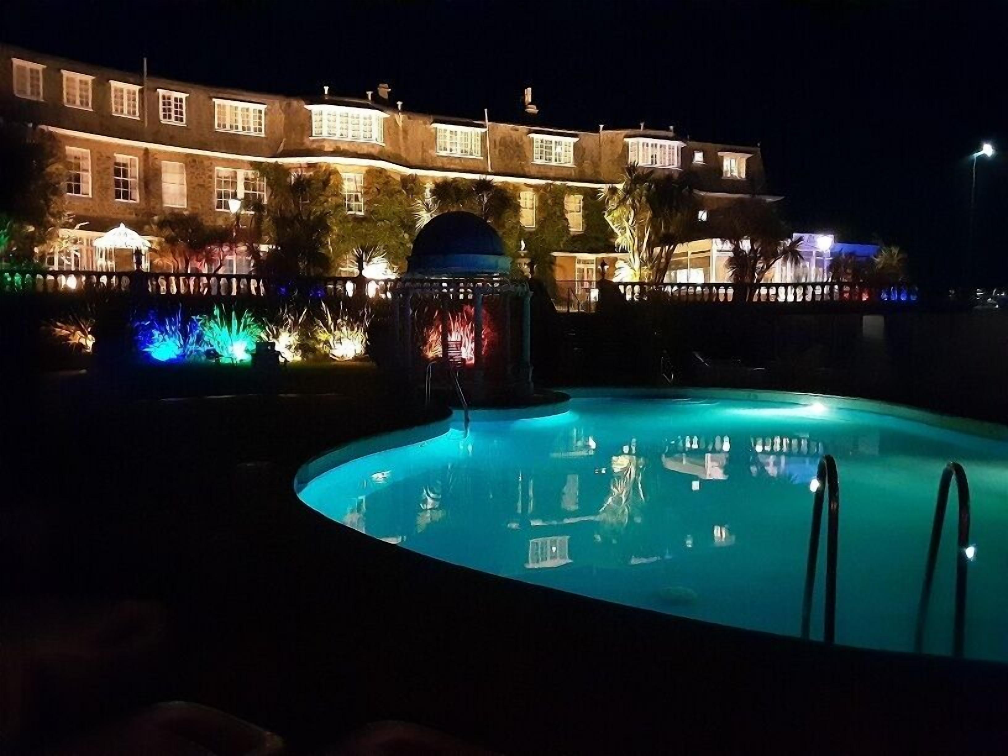 Vue nocturne d’un espace piscine avec un grand bâtiment en arrière-plan.