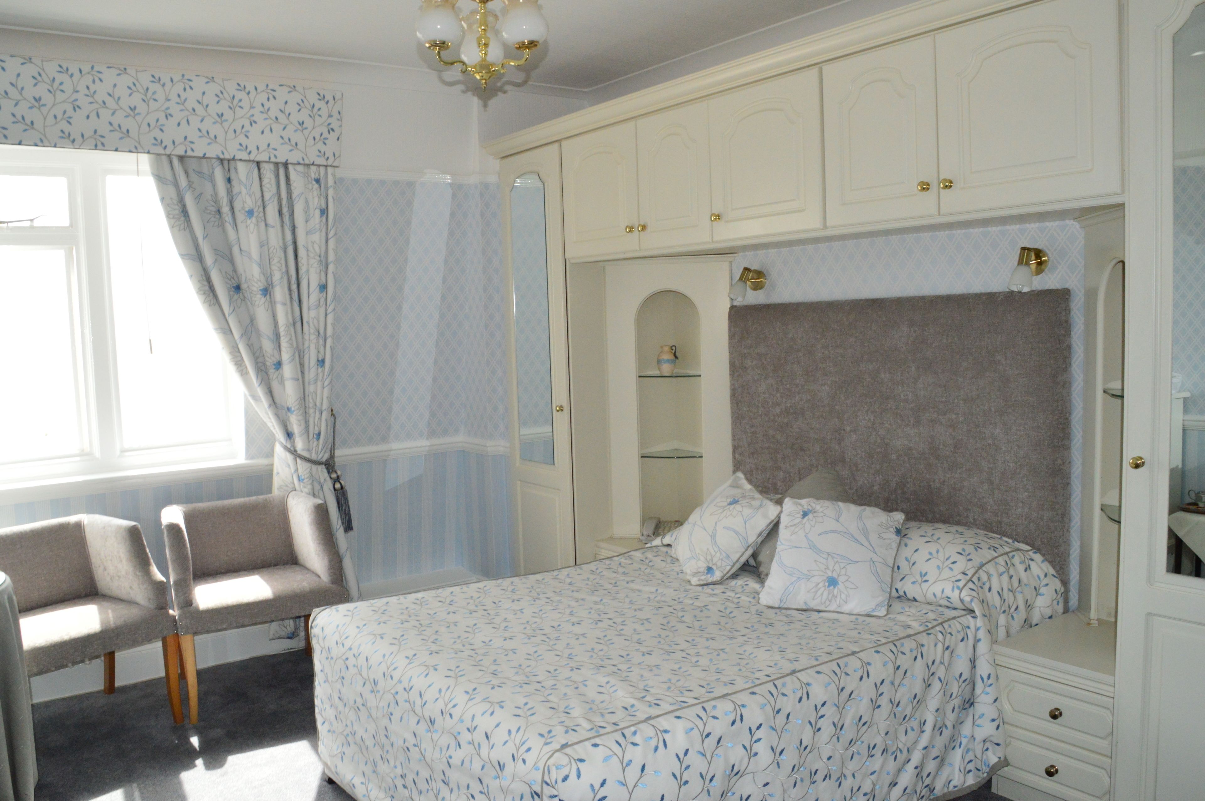 Une chambre à coucher comprenant un lit, une chaise, une armoire et une fenêtre avec des rideaux.
