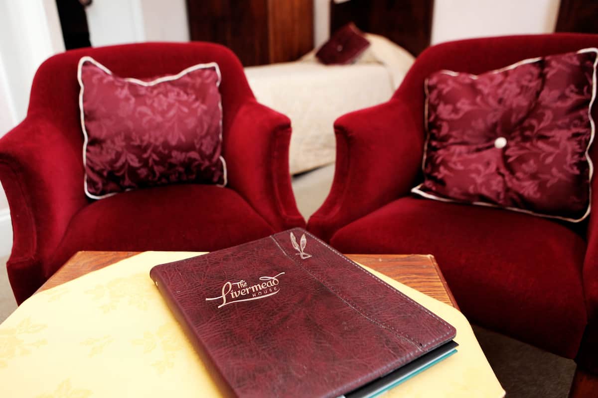Two red armchairs with matching pillows, a small wooden table, and a dark red leather-bound book titled "The Livermead House" on the table.