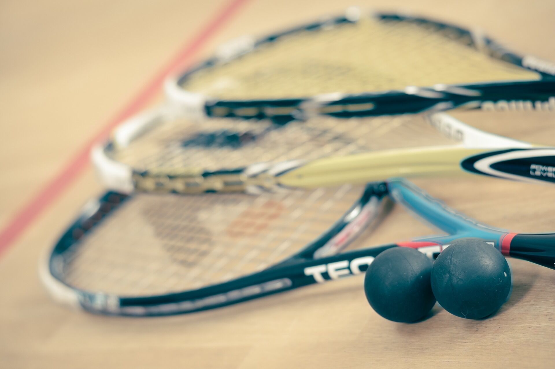 Een detailopname van twee tennisrackets met handgrepen en snaren, en twee tennisballen op een houten ondergrond.