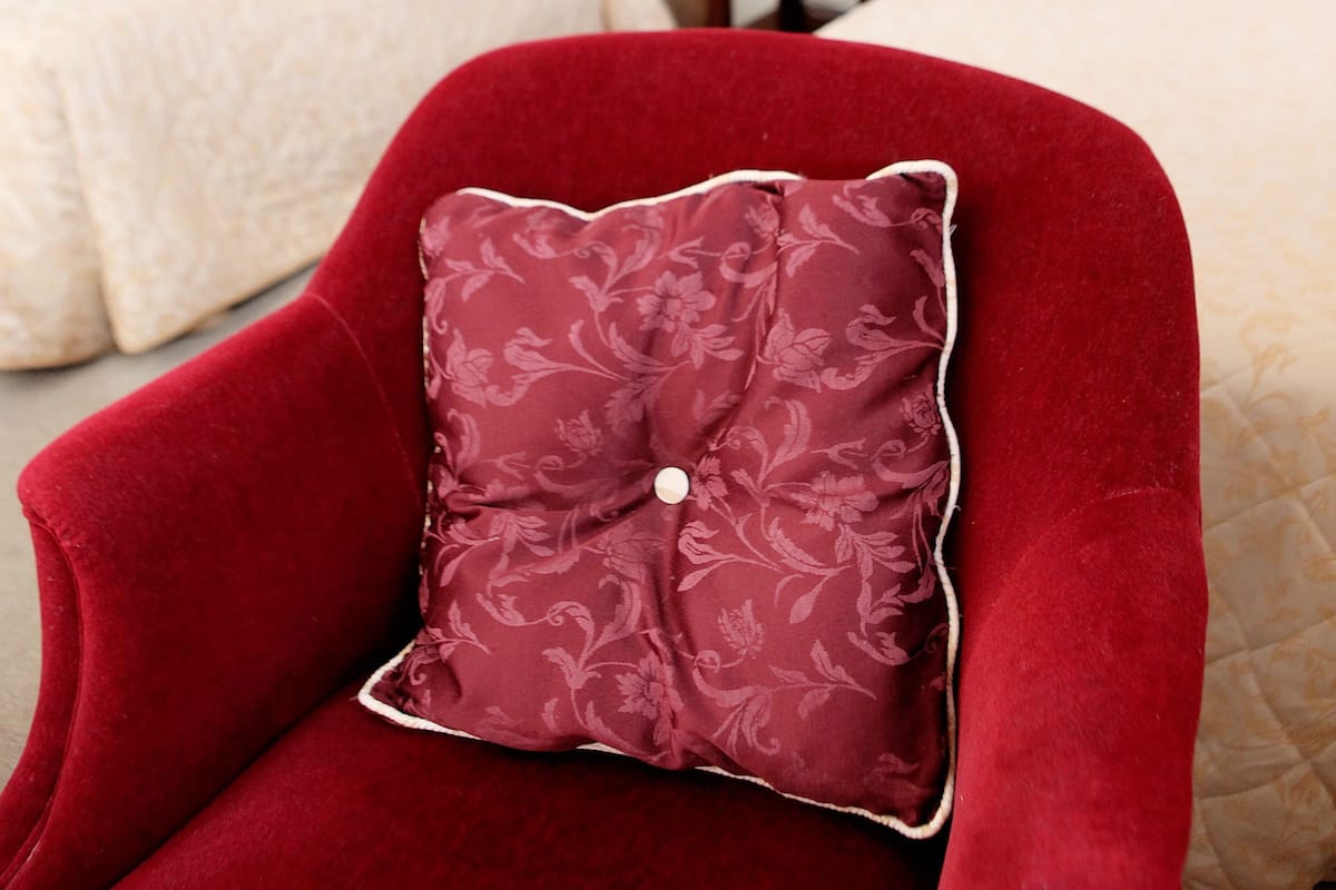 A hotel room with two beds, a wooden wardrobe, a nightstand, and a red armchair with a floral pillow.