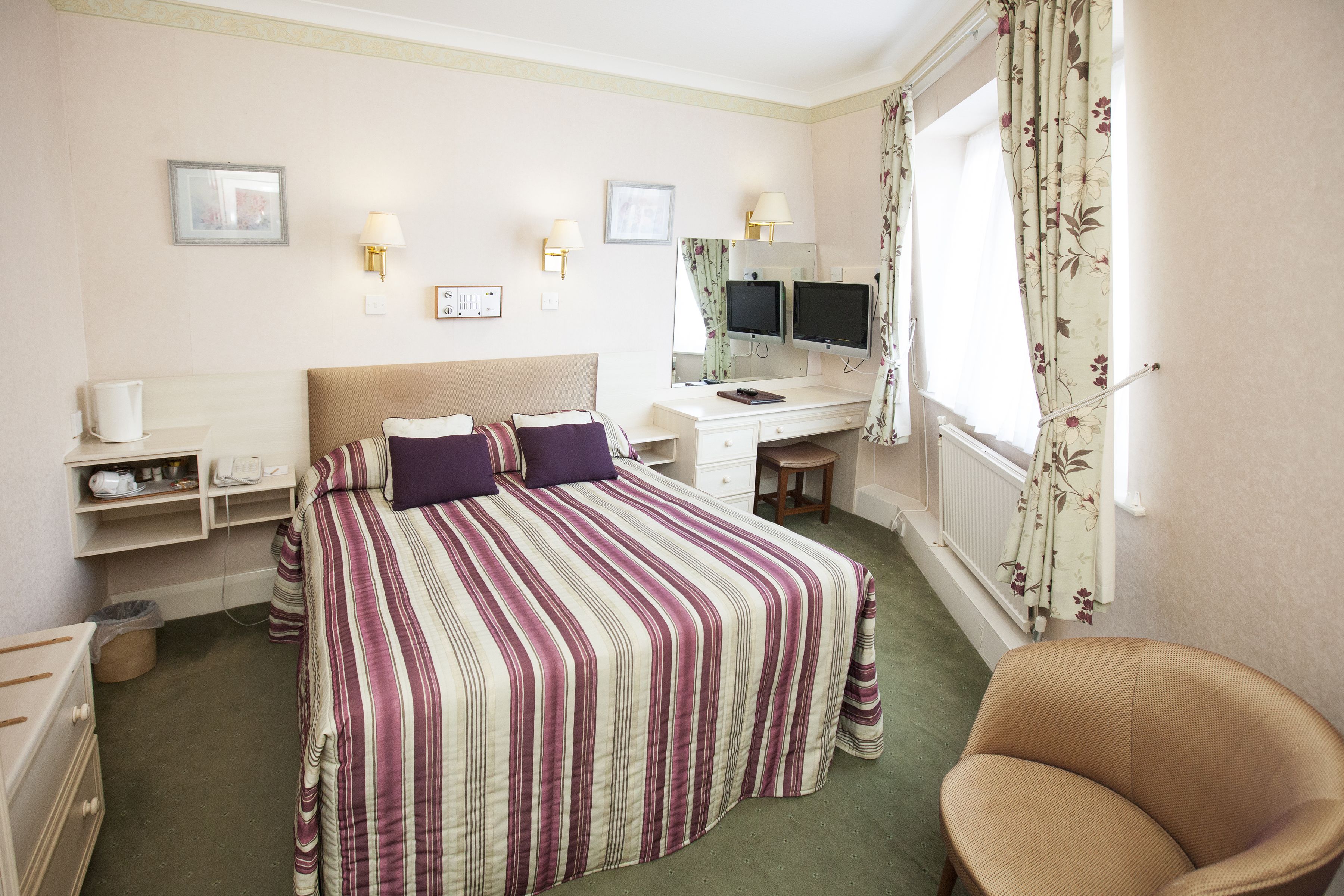 A hotel room with a bed, a desk with a computer, a chair, and a window with curtains.