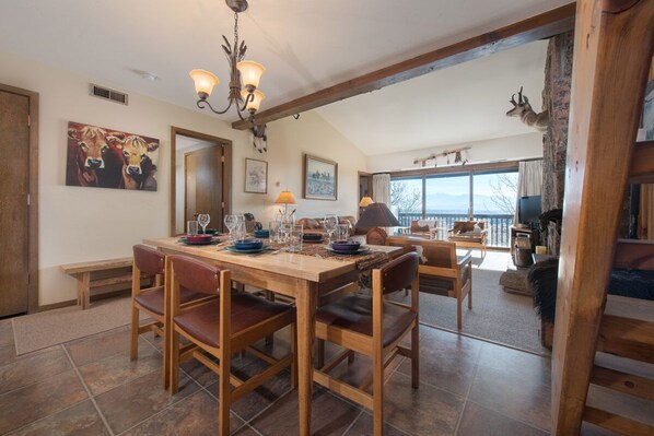 A dining area with a wooden table set for four, surrounded by chairs. There is a chandelier above the table, and a painting of cows on the wall. - JHRL - Whiteridge A4, Amazing location near Teton Village base (Teton Village)