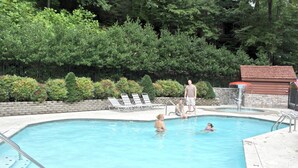 A swimming pool with lounge chairs, a hot tub, and a stone wall with greenery.